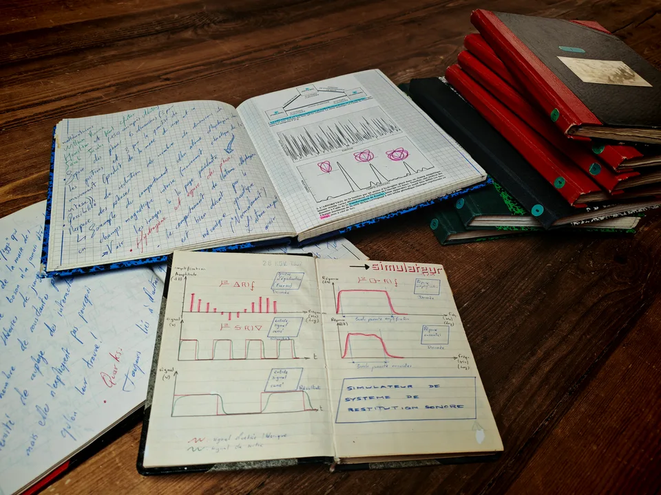 Carnets ouverts sur des notes et des schémas scientifiques, à côté d’une pile de volumes reliés.