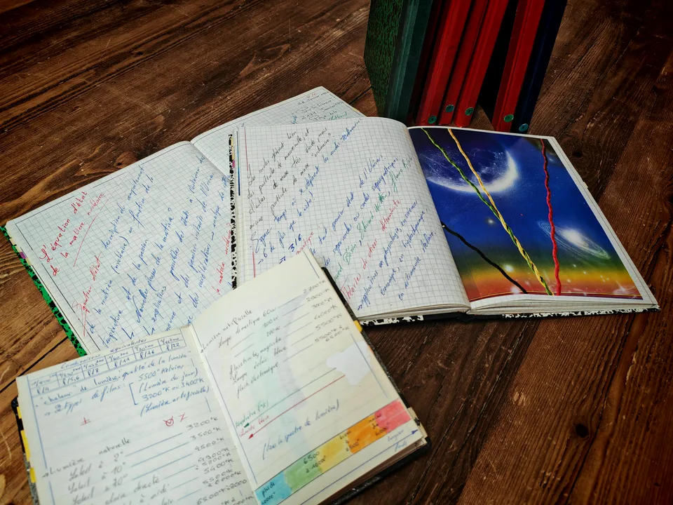 Pages manuscrites sur la matière et la lumière, illustration collée et carnets reliés dressés sur une table.